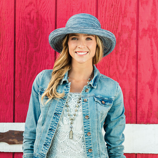 A stunning woman showcases this packable blue beach hat, offering both style and UPF 50+ sun protection. Recommended by the Skin Cancer Foundation, this wide-brimmed hat is both fashionable and functional, perfect for chic sun protection on any adventure.